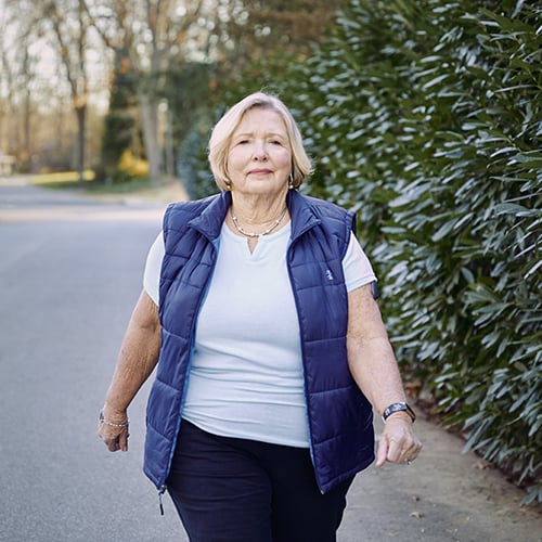 Mujer caminando al aire libre mientras lleva puesto el sistema de MCG Eversense con tecnología de sensor de glucosa.